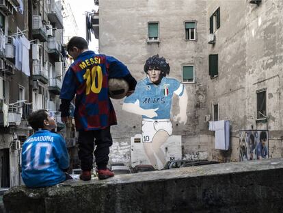 Dos niños con las camisetas de Messi y Maradona frente a un mural con la imagen del astro argentino en una calle de Nápoles.