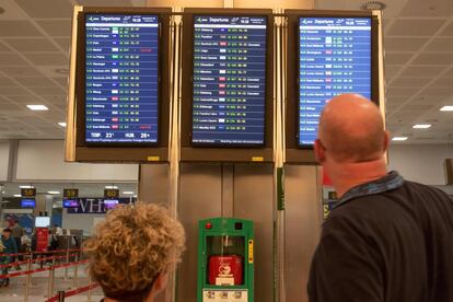 Dos personas miran la pantalla donde se muestran los vuelos cancelados y retrasados en el aereopuerto de Tenerife Sur.