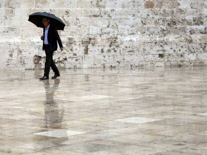 Un hombre, protegido con un paraguas, pasea por el casco antiguo deValencia.