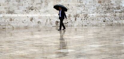 Un hombre, protegido con un paraguas, pasea por el casco antiguo deValencia.