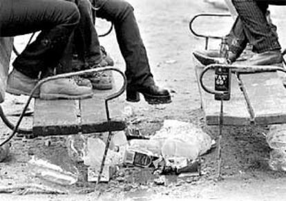 Unos jóvenes sentados en dos bancos, junto a restos de botellas de alcohol y vasos de plástico.