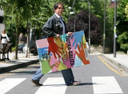 Suso del Toro, cruzando un paso de cebra próximo al campus de Santiago, con el cartel anunciador de su nuevo libro bajo el brazo.