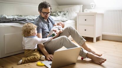 Un padre con dos niños mira un ordenador en su casa.
