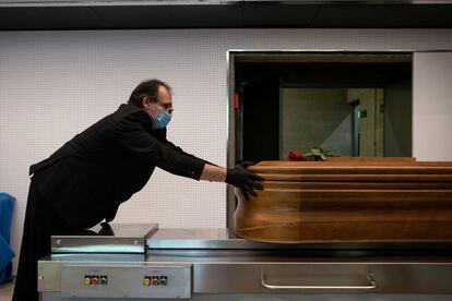 Un trabajador de la empresa funeraria Mémora introduce un ataúd en un horno crematorio. En el tanatorio de Girona, los cuerpos de los fallecidos confirmados o sospechosos de covid-19 son trasladados y desinfectados por personal con equipos de protección individual, antes de ser almacenados en una sala especial y aislada.