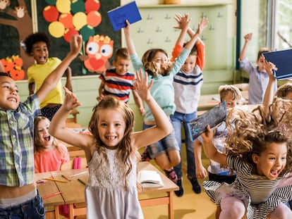 Large group of cheerful school children having fun while jumping among desks in the classroom.