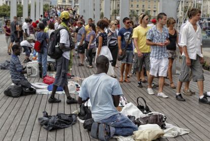 Un grupo de <i>manteros</i> vende bolsos y abanicos en La Rambla del Mar en Barcelona.