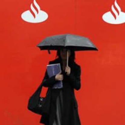 Una mujer con paraguas junto a unos logos del Banco Santander