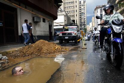 Un trabajador se ve parcialmente sumergido bajo el agua mientras trata de reparar una tuber&iacute;a rota en Caracas, Venezuela.