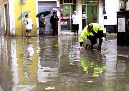 Un agente de la Policía Local de Sevilla trata de liberar un sumidero en una calle del centro de la ciudad.