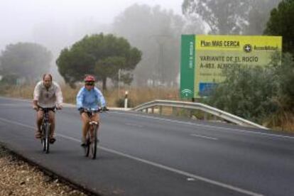 Dos ciclistas, junto a un cartel de una de las carreteras del entorno de Doñana.
