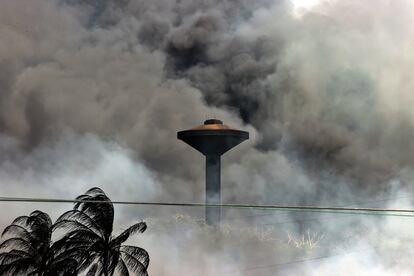 Un tanque para el almacenamiento de agua es visto delante de la columna de humo generada por el incendio, el lunes.