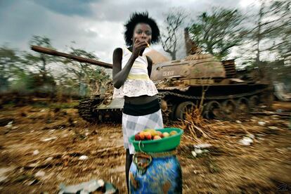 Una niña cruza cargada de fruta delante de un tanque del Movimiento Popular de Liberación de Angola (MPLA) abandonado que fue quemado por la UNITA durante la guerra civil en la aldea en Kwanza Norte.
