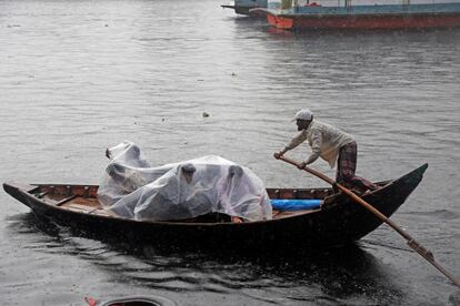 Varios pasajeros se protegen con plásticos de la lluvia mientras cruzan en bote el río Buriganga, en Dacca (Bangladés), este viernes.