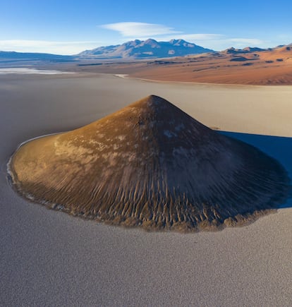 Quizá por su excelencia geométrica, quizá por su peculiar ubicación, el Cono de Arita (en la imagen) es un reclamo irrenunciable para quienes se adentran en el salar de Arizaro, de 1.600 kilómetros cuadrados de extensión, en la provincia argentina de Salta. Un capuchón de origen volcánico —está compuesto de sal y lava negra— que rompe el árido paisaje del tercer desierto de sal más grande de Sudamérica, después de Uyuni (Bolivia) y Atacama (Chile). El vértice de esta pirámide natural perfecta que se eleva unos 200 metros sobre este níveo altiplano de la Puna argentina, hasta alcanzar los 3.689 metros de altitud, permanece virgen. Aunque son frecuentes los grupos turísticos que llegan hasta su base en excursiones de uno o varios días desde Salta, la capital provincial, con parada habitualmente en la localidad de Tolar Grande, a 80 kilómetros de distancia, ningún visitante se atreve a escalar hasta la punta del cono: se trata de una geoforma sagrada según la tradición indígena. En lengua aimara, Arita significa, precisamente, punzante.
