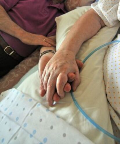 Un hombre toma la mano de su esposa, a la que cuida.