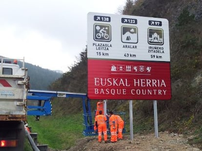 Operarios colocan un cartel con el lema 'Euskal Herria-Basque Country' en la carretera que une Gipuzkoa con Navarra.