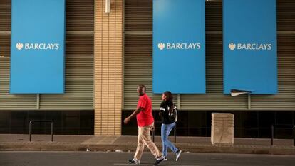 Dos personas pasan por delante de tres logos de Barclays y Johannesburgo (Sud&aacute;frica).