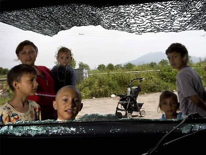 Unos niños miran por la ventanilla rota de un coche en el campamento gitano de Casoria (Nápoles).