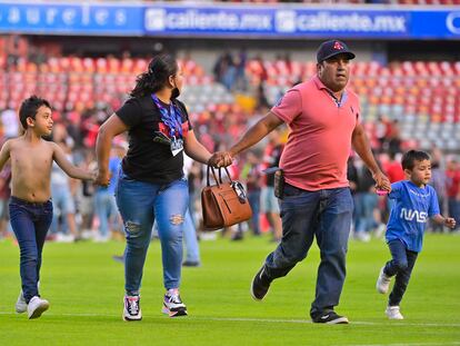 Una familia corre durante el enfrentamiento entre los aficionados del Querétaro y el Atlas en el estadio Corregidora.