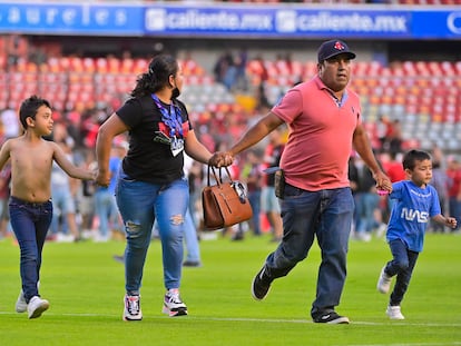 Una familia corre durante el enfrentamiento entre los aficionados del Querétaro y el Atlas en el estadio Corregidora.