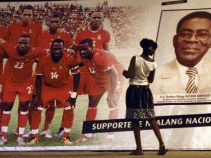 Una mujer mira un p&oacute;ster de la selecci&oacute;n de f&uacute;tbol de Guinea Ecuatorial junto al presidente Obiang.