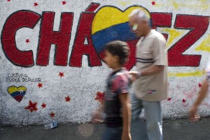 Dos transe&uacute;ntes caminan frente a un grafiti a favor de Ch&aacute;vez. 