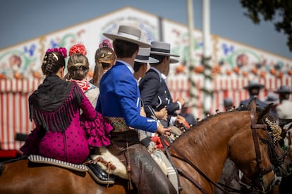 Tres jinetes con tres mujeres vestidas de flamenca a caballo.