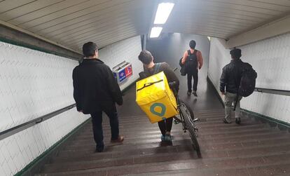 Un joven baja las escaleras de una estación de metro de Madrid con una bicicleta de reparto de pedidos a domicilio.