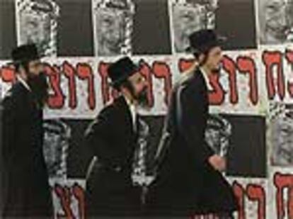 Tres judíos de una secta ortodoxa caminan por una calle de Jerusalén ante un cartel de Arafat en el que se lee en hebreo "asesino".