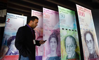 Un hombre camina frente a una publicidad sobre el bol&iacute;var.