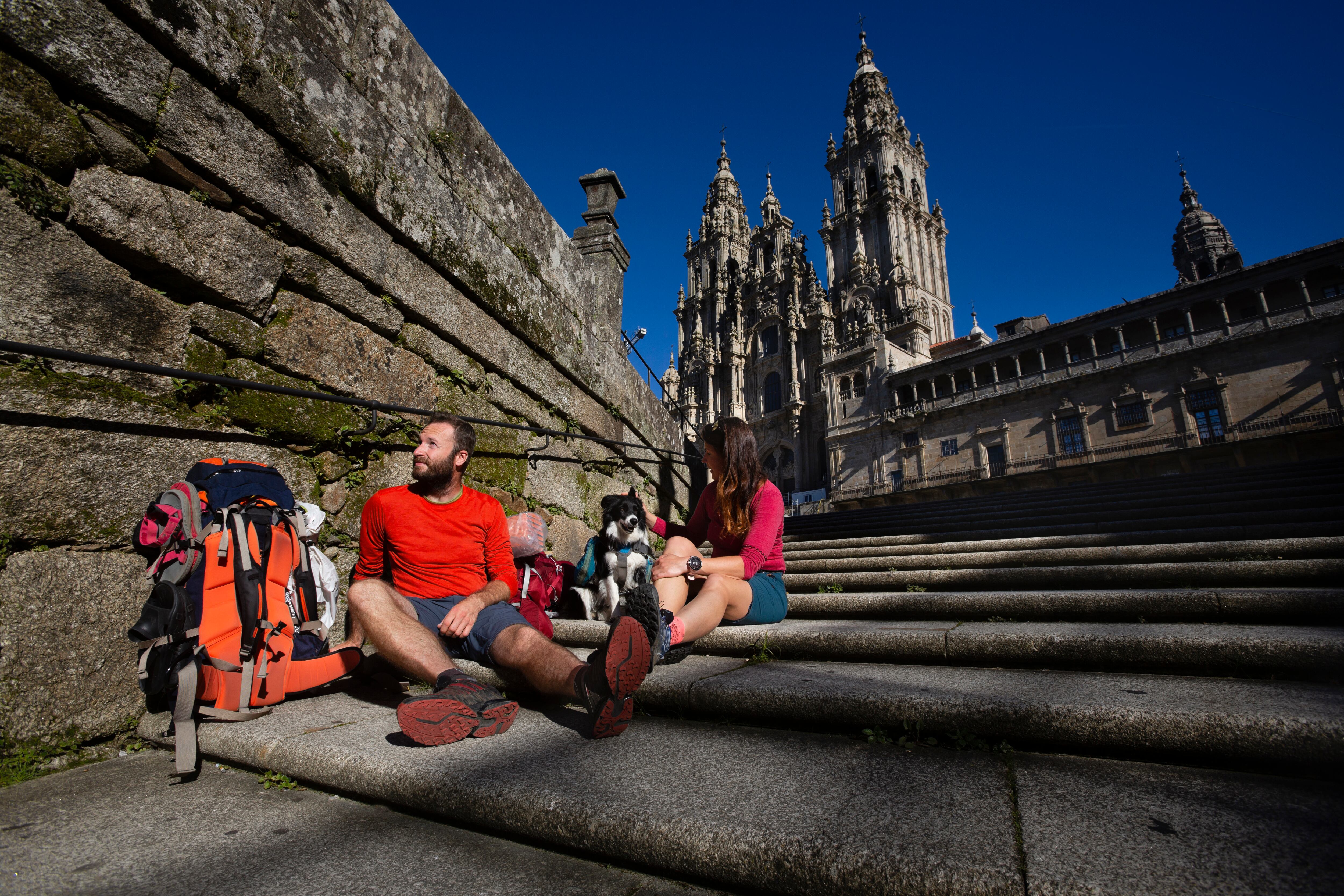 Dos peregrinos terminan el Camino de Santiago y descansan en las escaleras de la Plaza del Obradoiro en frente de La Catedral. 