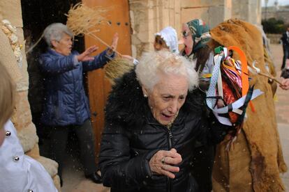 Dos mujeres salen de la iglesias mientras dos participales del carnaval "El gallo de carnval" les lanzan plumas y resina, en Mecerreyes (Burgos). Es una fiesta pagana en los que participan personas cantando , bailando y atacar el ' Gallo ' que se defiende por Zarramacos .