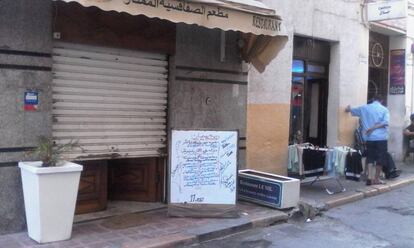 Un restaurante del centro de Túnez con la persiana medio bajada, pero un menú frente a la puerta.