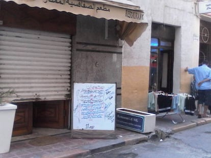 Un restaurante del centro de Túnez con la persiana medio bajada, pero un menú frente a la puerta.