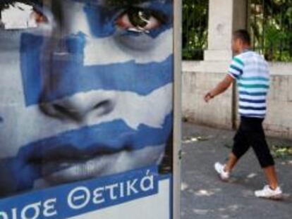 Un peatón pasa delante de un cartel que invita a votar a los griegos
