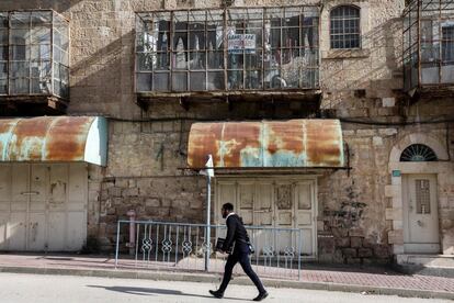 Un israelí pasa junto a una casa palestina, con la terraza cubierta por mallas y un cartel de protesta que dice en inglés "Los árabes están prohibidos, esta es la calle Apartheid", en la calle Shuhada de Hebrón, en la zona controlada por Israel, el 28 de enero.