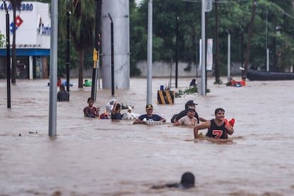 Personas cruzan una avenida inundada por el paso del huracán 'John' en la parte alta del puerto de Acapulco.