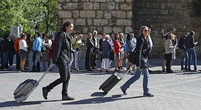 Dos mujeres pasan con sus maletas junto al Alc&aacute;zar de Sevilla.