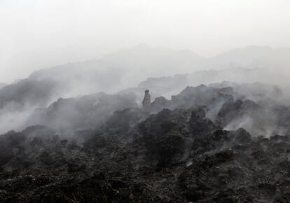 Una mujer recoge materiales entre nubes de humo de un basurero en llamas en las afueras de Ahmedabad (India).  