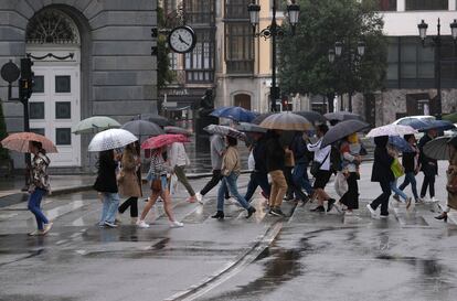 Varias personas cruzan un paseo de peatones protegidas con paraguas, junto al Teatro Campoamor de Oviedo, este sábado.