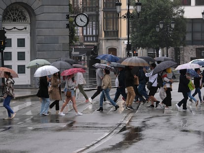 Varias personas cruzan un paseo de peatones protegidas con paraguas, junto al Teatro Campoamor de Oviedo, este sábado.