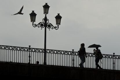 La llegada de la lluvia está dejando calles anegadas, inundaciones en bajos, daños en vehículos y cortes de luz en el oeste de Andalucía. En la imagen, un chico en el Puente de Triana en Sevilla, se protege de la lluvia con un paraguas, el 17 de octubre de 2017.