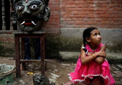 Una niña se sienta al lado de la efigie del demonio Ghantakarna, antes de que esta sea quemada para simbolizar la destrucción del mal y la creencia de conducir espíritus malignos y fantasmas, durante el festival Ghantakarna en Bhaktapur (Nepal), este martes.