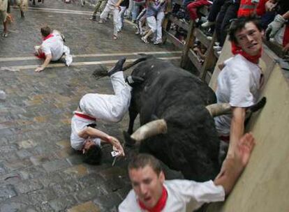 Un <i>miura</i> coge a tres corredores en la curva de Mercaderes, ayer en Pamplona.