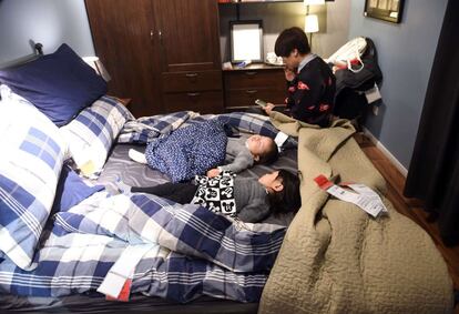Una mujer cuida el sueño de sus hijos, que duermen en una cama expuesta en una tienda de muebles en Pekín (China).