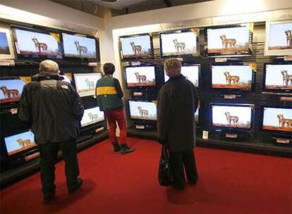 Tres clientes observan televisores en un establecimiento comercial donostiarra.