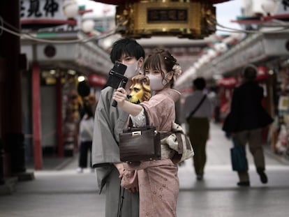 Visitantes protegidos con mascarillas se toman selfis en un centro comercial del distrito de Asakusa, en Tokio (Japón).