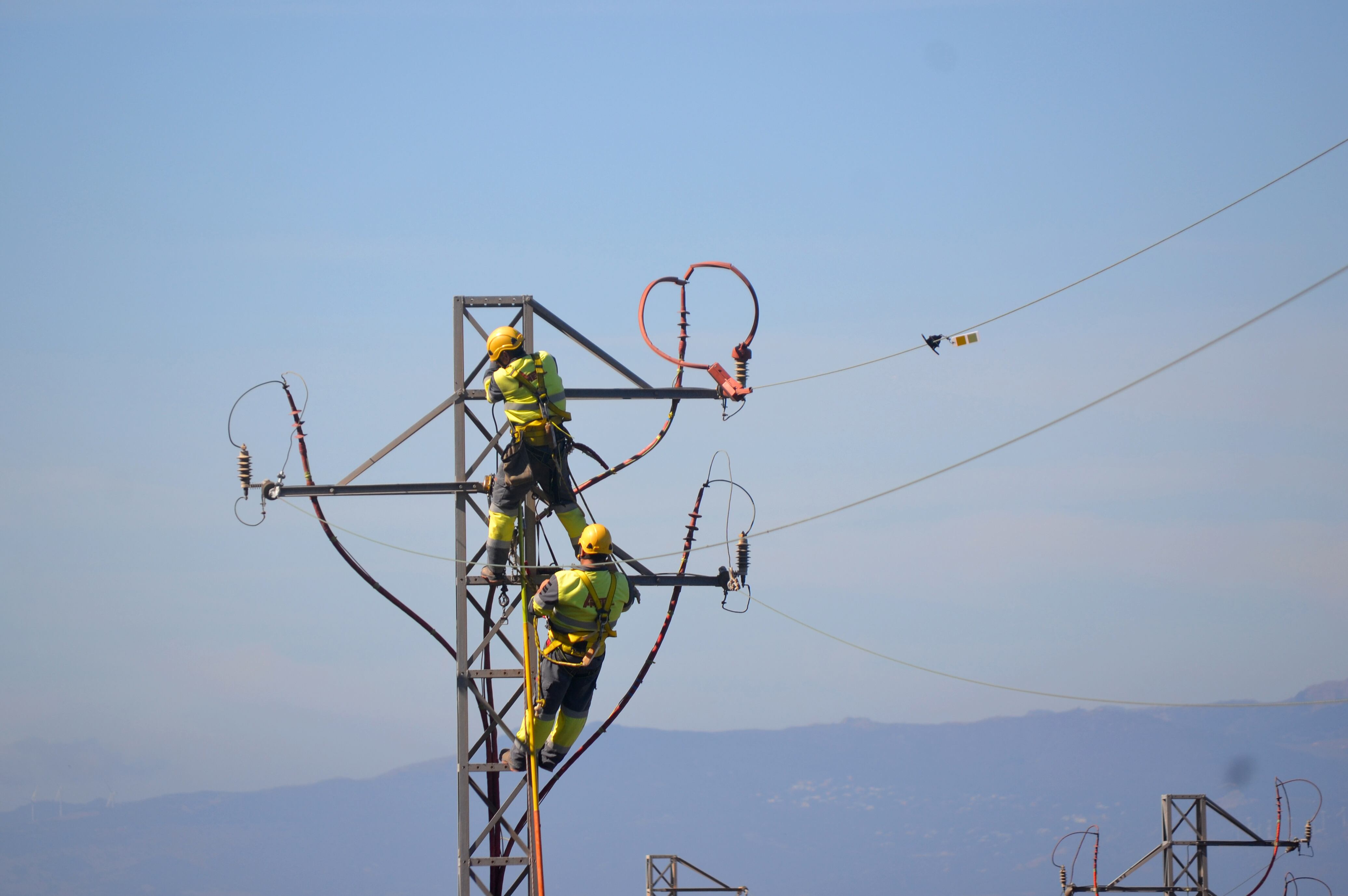 Dos hombres trabajan en una torreta eléctrica. 