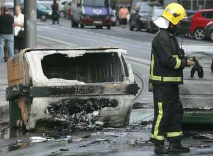Un operario de Bomberos analiza los destrozos junto a un contenedor quemado en una calle de Bilbao.
