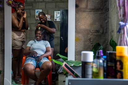 Una peluquera hace trenzas y extensiones a una mujer antes de que empiecen las Adoraciones al Niño Dios Negro.